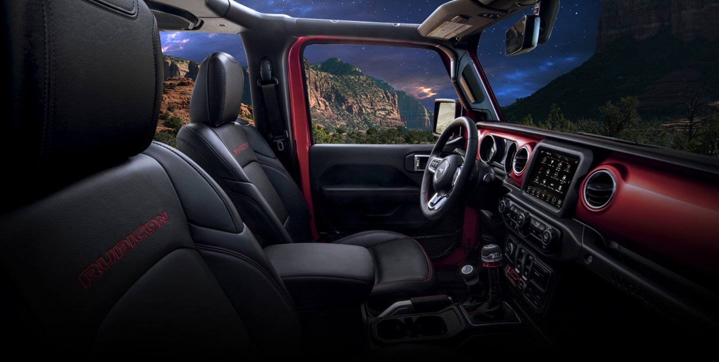 The interior of Jeep Wrangler Sahara focusing on the steering wheel, entertainment center and dashboard.