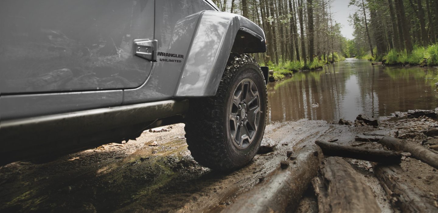 Close-up of Jeep Wrangler wheel as vehicle is being driven on muddy terrain.