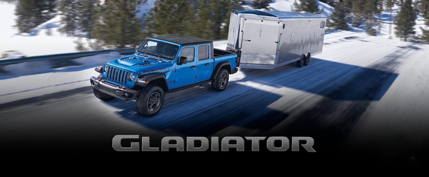 The 2022 Jeep Gladiator Rubicon towing an enclosed trailer on a snowy mountain road. The Presidents Day Event logo.